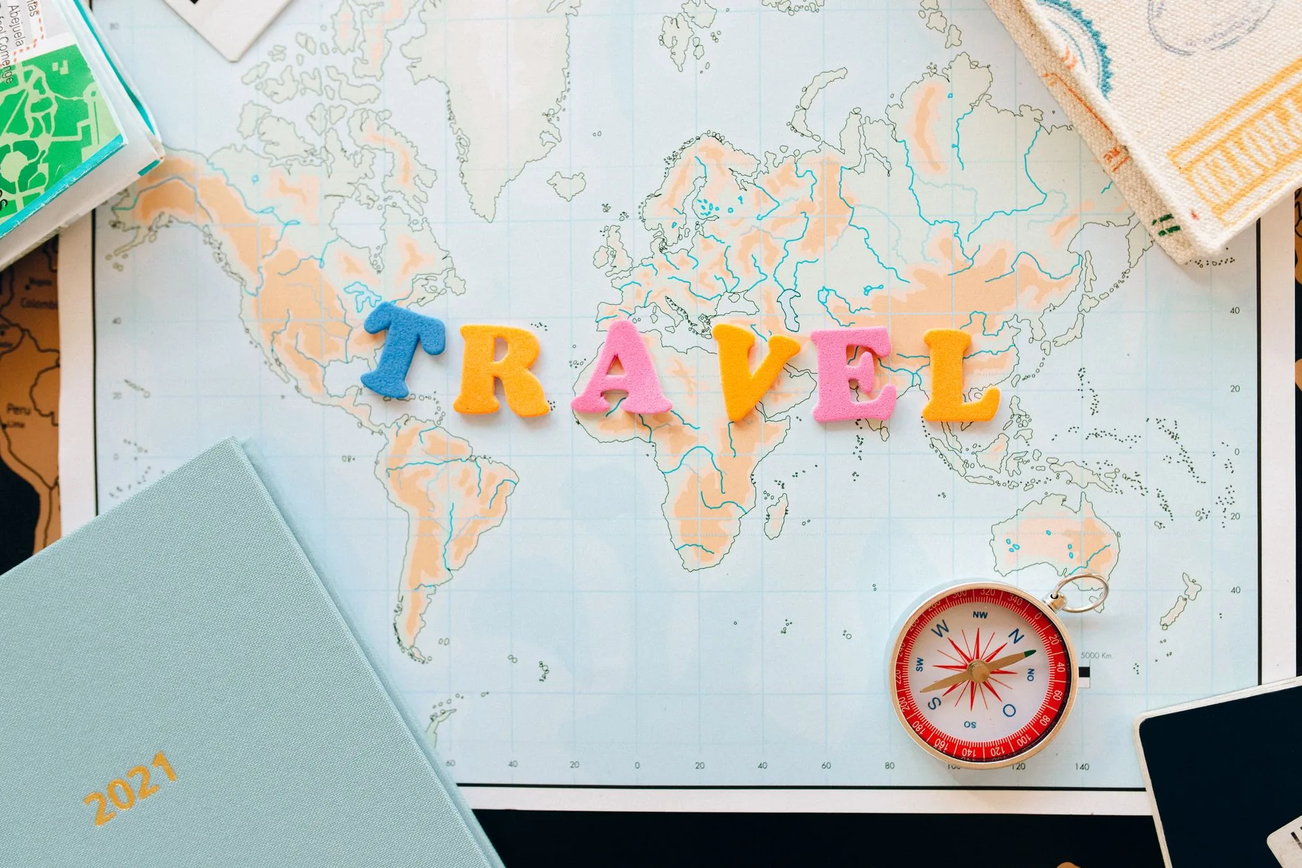 Flat lay of a map with colorful letters "TRAVEL" and a compass for planning adventures. 说明图