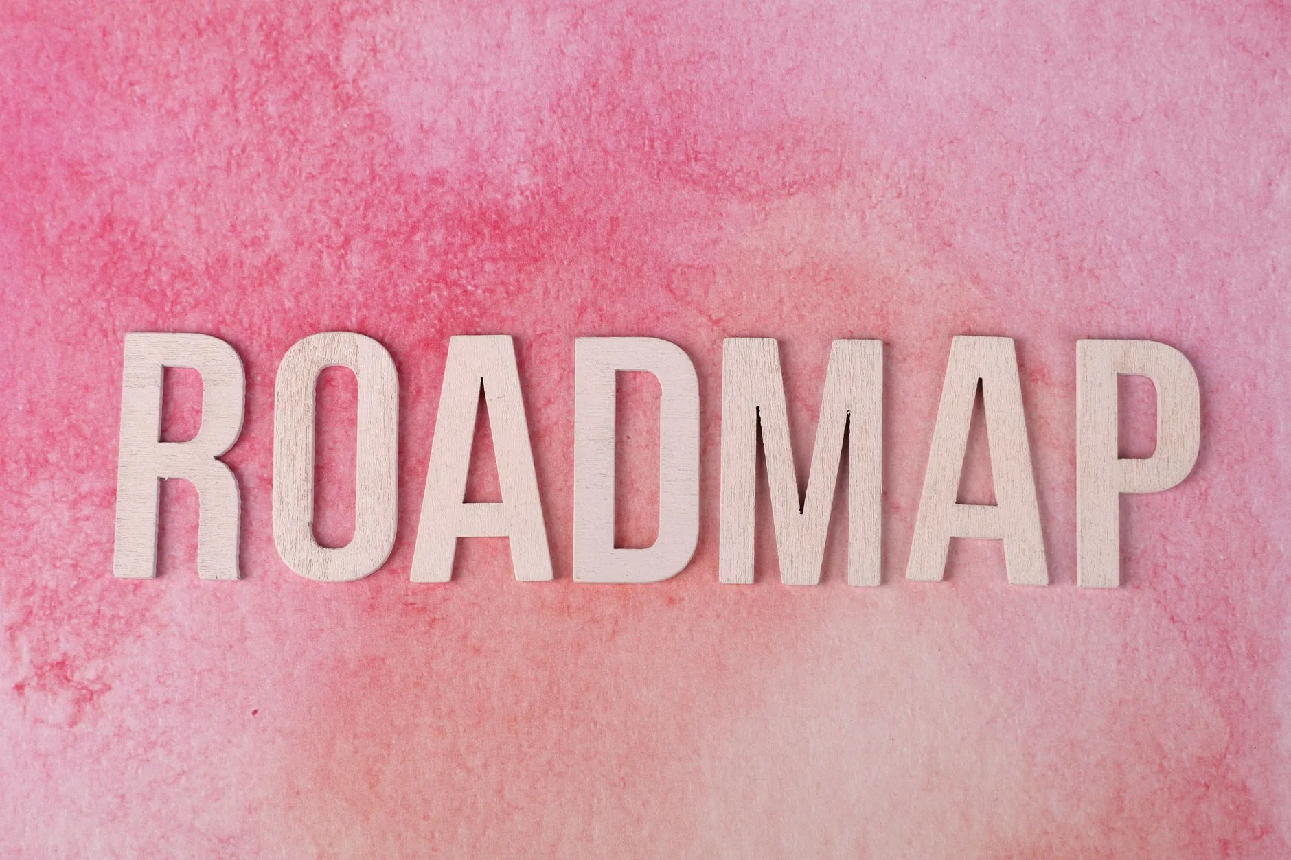Wooden letters spelling 'ROADMAP' on a vibrant pink watercolor background. 说明图
