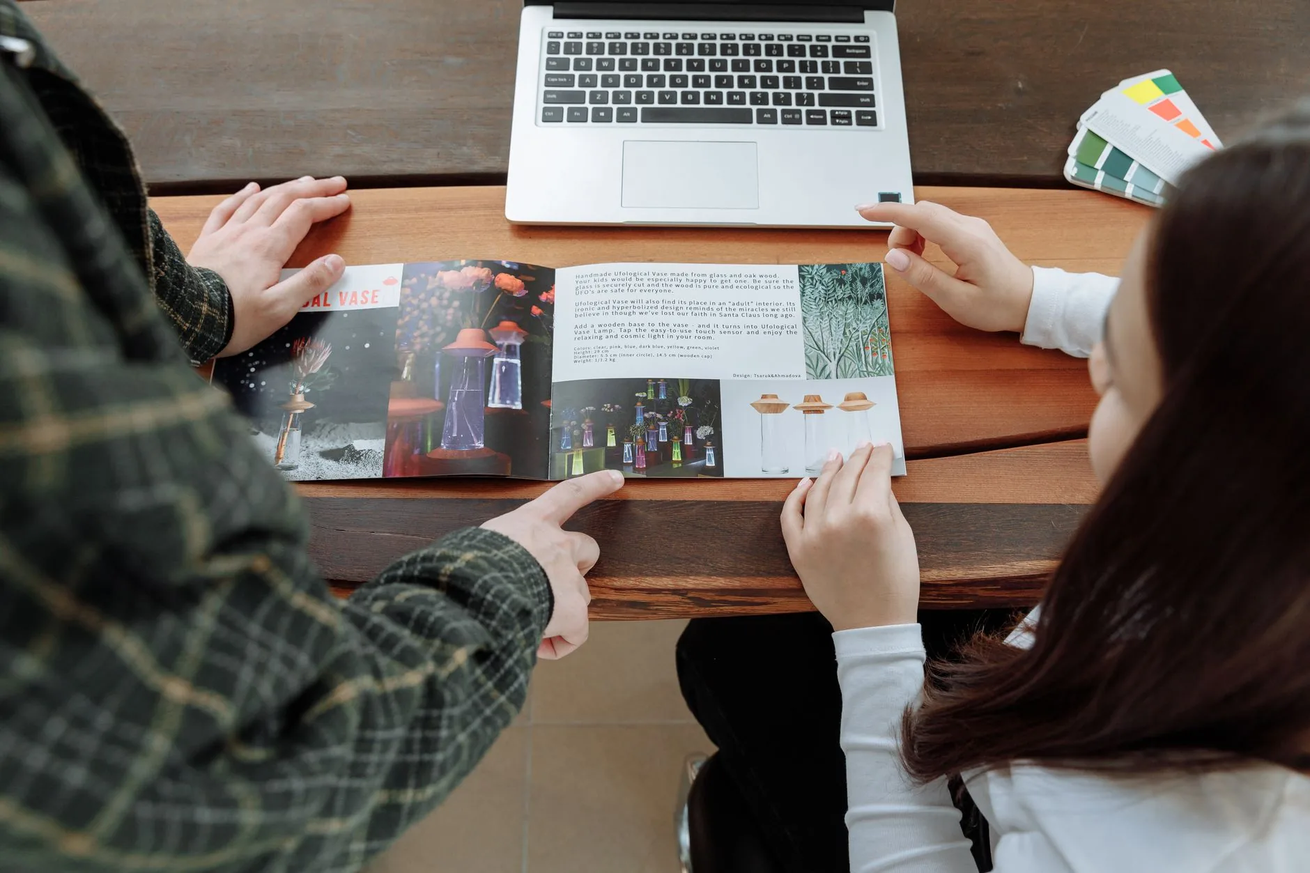 Two people reviewing a design brochure at a collaborative workspace with a laptop. 说明图
